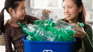 Mum and daughter recycling green plastic bottles